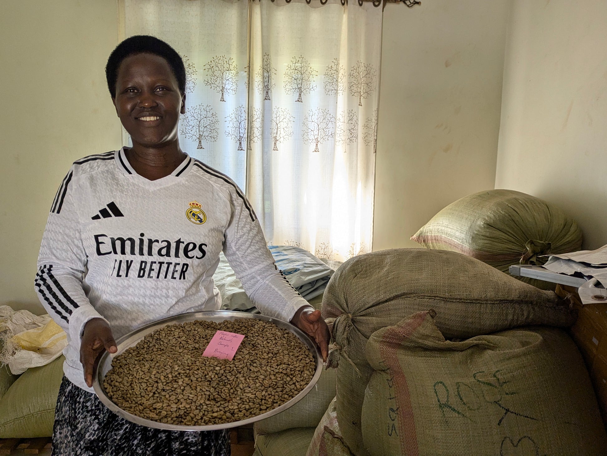 Woman holding a tray of beans in a room with coffee sacks.