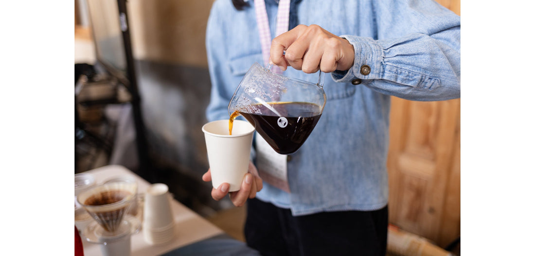 Closeup of person pouring coffee from a glass carafe into a paper cup