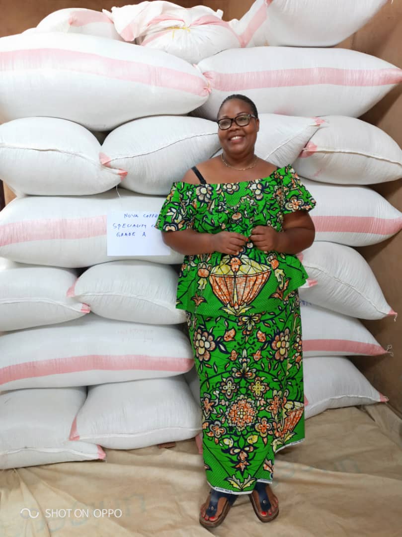 Woman in green dress standing in front of sacks of coffee