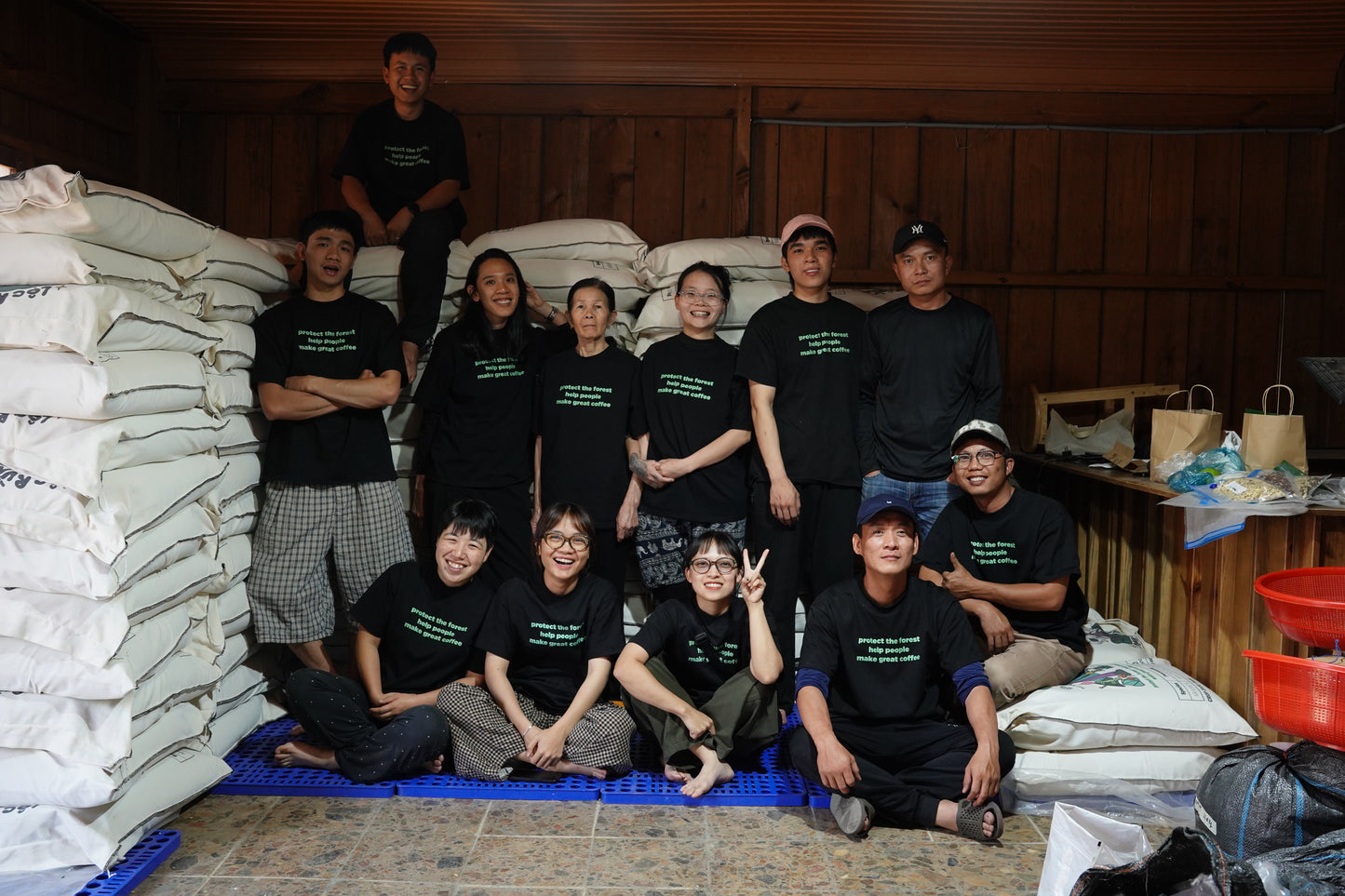 Team of twelve people posing next to a stack of coffee bags in a warehouse